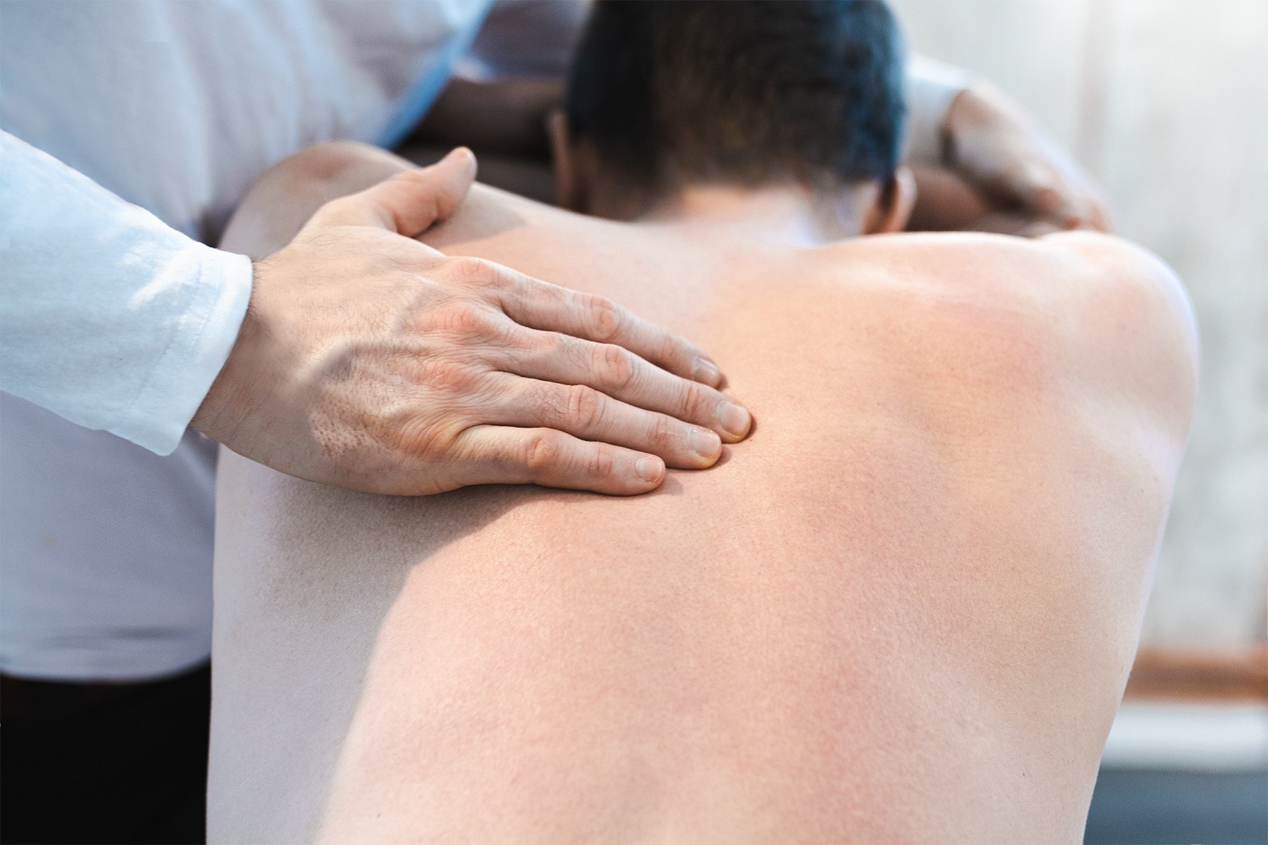 Osteopath Gunanr Sinnig behandelt mit seinen Händen den oberen Rückenbereich seines Patienten